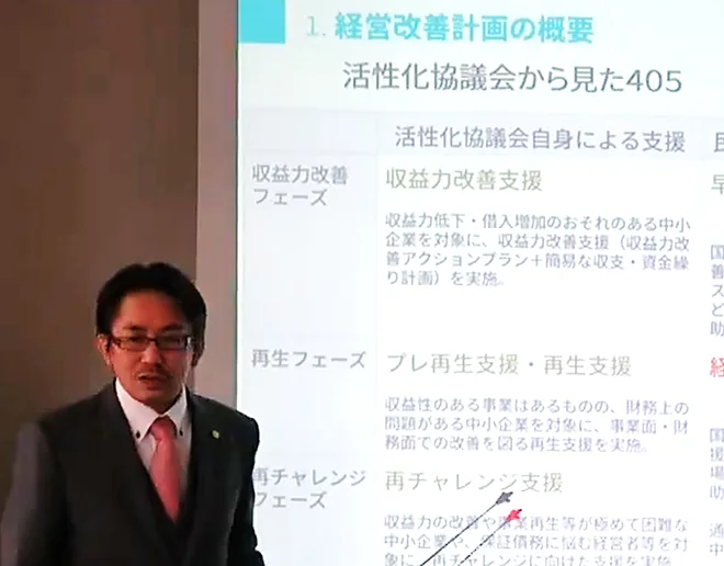 スクリーンに映した経営改善計画の資料を差し棒で示しながら話す西達郎
